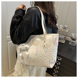 Detail of white quilted tote bag with colorful wavy embroidery and plush cloud charm