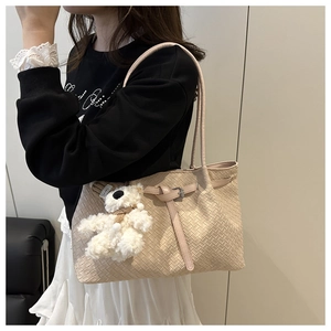 Detail of beige woven tote bag with a decorative strap and cute teddy bear charm