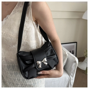 Detail of a black pleated underarm bag featuring a large bow and silver metal buckle