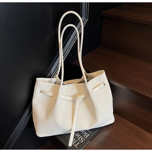 Gros plan d'un sac seau blanc à texture tressée sur un escalier avec double sangle