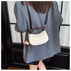 Détail du sac bandoulière blanc cassé avec logo doré et breloque gant de baseball stylée
