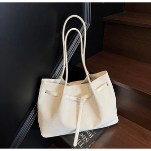 Détail d'un sac cabas tressé crème avec lanière en cuir et boucle métallique décorative