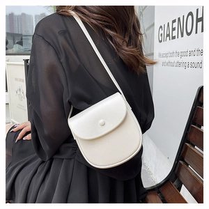 Close-up of a white leather saddle bag with a round buckle on a crossbody shoulder strap