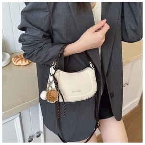 Détail du sac demi-lune blanc cassé avec breloques de baseball et bandoulière marron