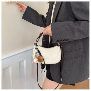 Détail du sac demi-lune crème avec lettrage doré et accessoire pendentif de baseball