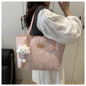 Detail of pink embroidered tote bag with textured E-pattern and plush cloud charm accessory