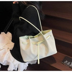 Détail du sac seau en cuir texturé jaune clair avec boucle décorative et fine bandoulière