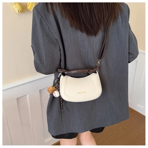 Détail du sac bandoulière demi-lune blanc cassé avec sangle marron et breloque baseball