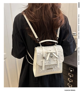 Detail of white lace backpack featuring heart pendant and metallic fashion logo