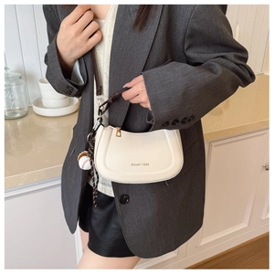 White minimalist half-moon crossbody bag featuring a baseball charm on adjustable strap