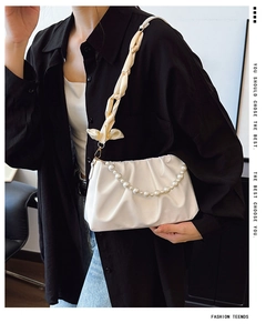 Close-up of white pleated cloud bag featuring pearl handle and woven shoulder strap details