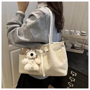 Détail d'un sac bandoulière tressé crème avec pendentif ours en peluche et boucle