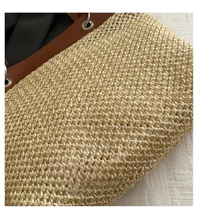 Close-up detail of woven straw tote bag with brown leather trim and silver metal eyelets