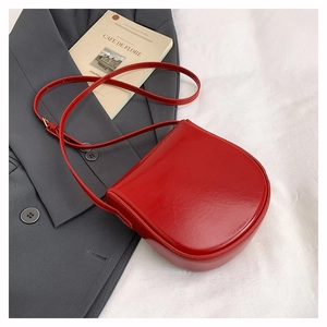 Close-up of a red leather saddle bag with adjustable strap on a grey blazer background