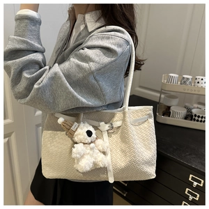 Detail of white woven tote bag with plush bear charm and metallic buckle closure