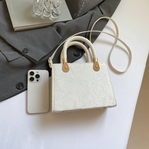 White lace floral crossbody mini bag with woven handle and gold hardware on a desk
