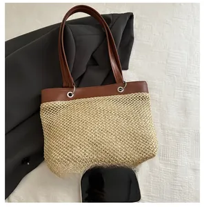 Detail view of woven straw tote bag with brown leather handles and metallic eyelets
