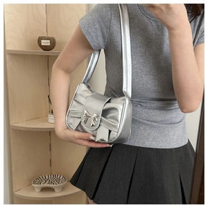 Close-up of silver pleated underarm bag with metallic bow detail and glossy finish