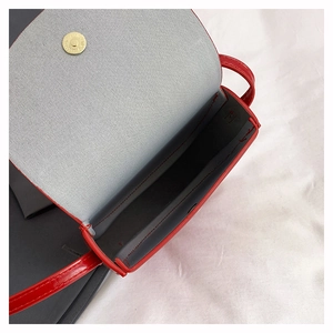 Close-up of red glossy saddle bag showing gray lining and golden magnetic snap closure