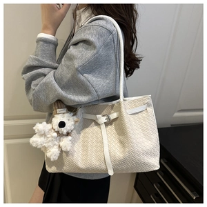 Detail of woven tote bag with silver buckle and cute teddy bear pendant on shoulder strap