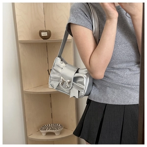 Detail of silver metallic underarm bag featuring pleats and a decorative bow ornament