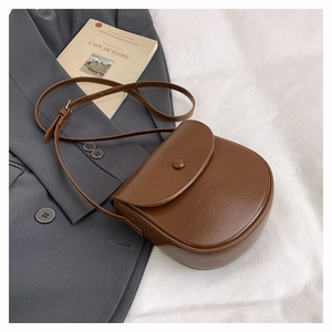 Top-down shot of a brown saddle bag on a grey blazer with a decorative book
