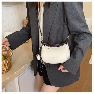 Side view of a beige half-moon crossbody bag with a brown strap and baseball charm