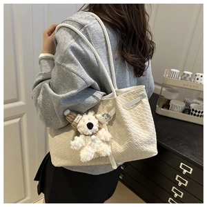 Detail of cream woven tote bag featuring a plush bear charm and leather strap accents