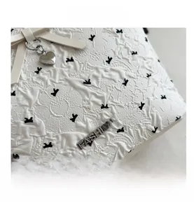 Macro detail of white textured bag featuring black bow patterns and a heart pendant charm
