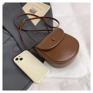 Flat lay of a brown leather saddle bag on a grey blazer with a white smartphone
