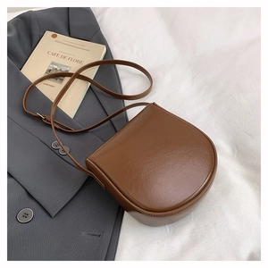 Brown leather saddle bag displayed on white fabric with a blazer and vintage book