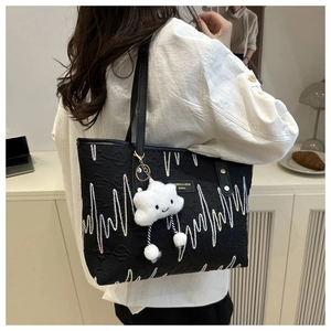 Detail view of black canvas tote bag with wave embroidery and white cloud charm