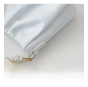 Close-up of golden metal hook and elegant pearl chain detail on white pleated bag