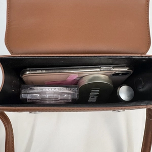 Brown faux leather crossbody bag showing interior capacity with phone and cosmetics