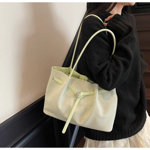 Vue latérale d'un sac seau vert clair texturé porté par un mannequin en tenue décontractée
