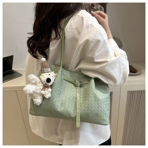 Detail of light green woven tote bag with adjustable strap and fluffy bear pendant charm