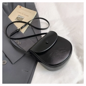 Detail of a black leather saddle bag with gold metal buckle on a grey suit background