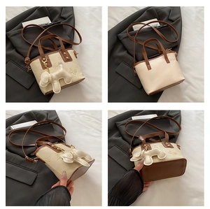 Vista detallada del bolso saco crema con relieve de mariposa y colgante de perrito