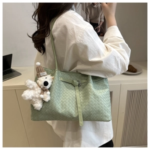 Detail of light green woven tote bag featuring a decorative leather strap and plush bear charm