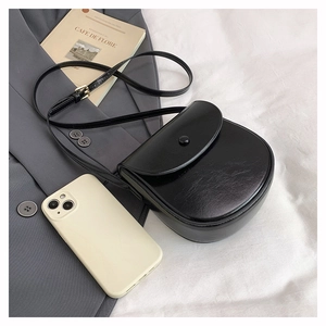 Flat lay of a minimalist black saddle bag with gold hardware on a white fabric backdrop