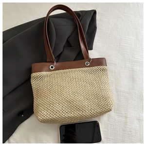 Detailed close-up of beige straw tote bag with brown faux leather handles and metal eyelets
