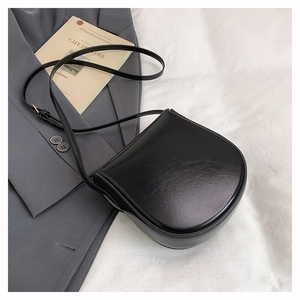 Flat lay of a minimalist black saddle bag with adjustable gold buckle on a stylish gray blazer