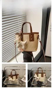 Detalle del bolso de cubo blanco crema con relieve de mariposa y colgante de perro