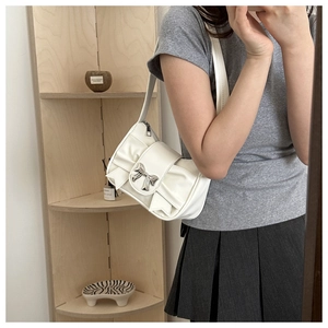 Detail of white pleated shoulder bag featuring layers of bows and a silver metal buckle