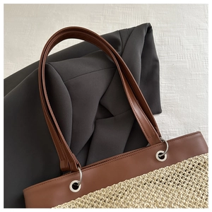 Close-up of woven straw handbag with brown leather handles and silver metal grommets