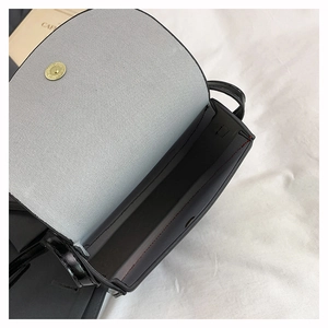 Close-up of black saddle bag with magnetic buckle closure on white fabric background