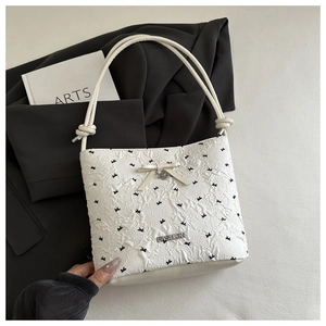 Detail of white quilted tote bag featuring black bow patterns and elegant beige bow pendant