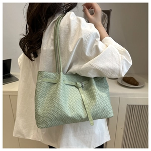 Detail of mint green woven tote bag on shoulder showing texture and metallic strap buckle