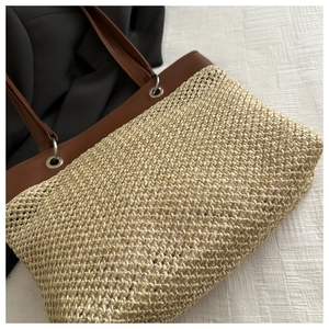 Detail of woven straw tote bag with brown leather handles and silver metal grommets