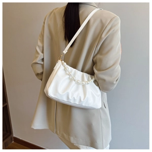 Detail of white pleated cloud bag with pearl chain shown on a woman in a beige blazer